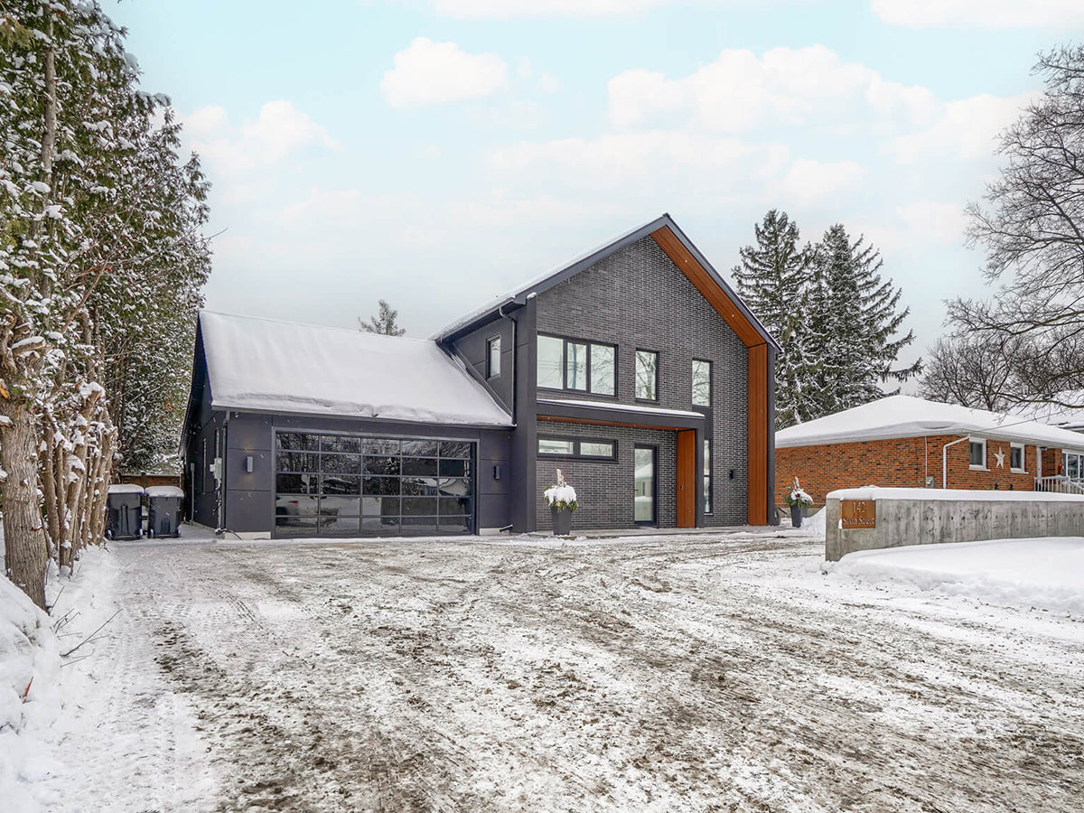 Front exterior of contemporary black brick house with gable roof and garage in winter.