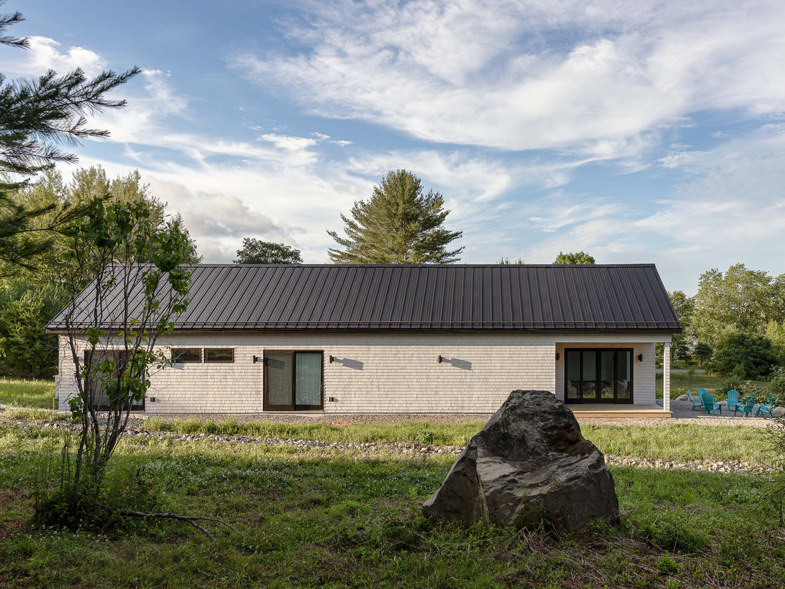 Cedar shingle modern farmhouse exterior in Monroe Maine — white bleached cedar siding with black metal roof and gabled porch entry