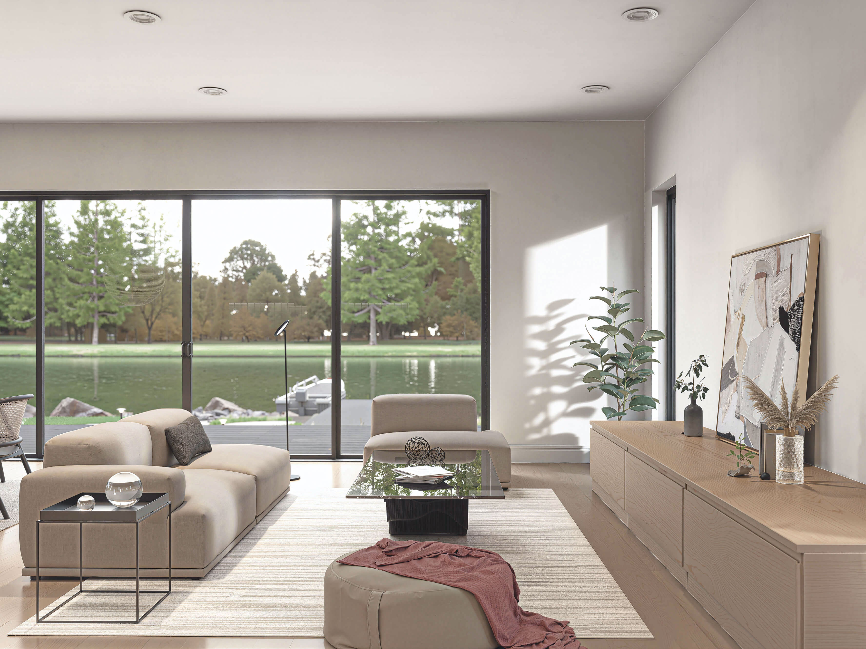 Barndominium house plan living room with floor-to-ceiling sliding glass doors overlooking waterfront, neutral sectional sofa and oak credenza