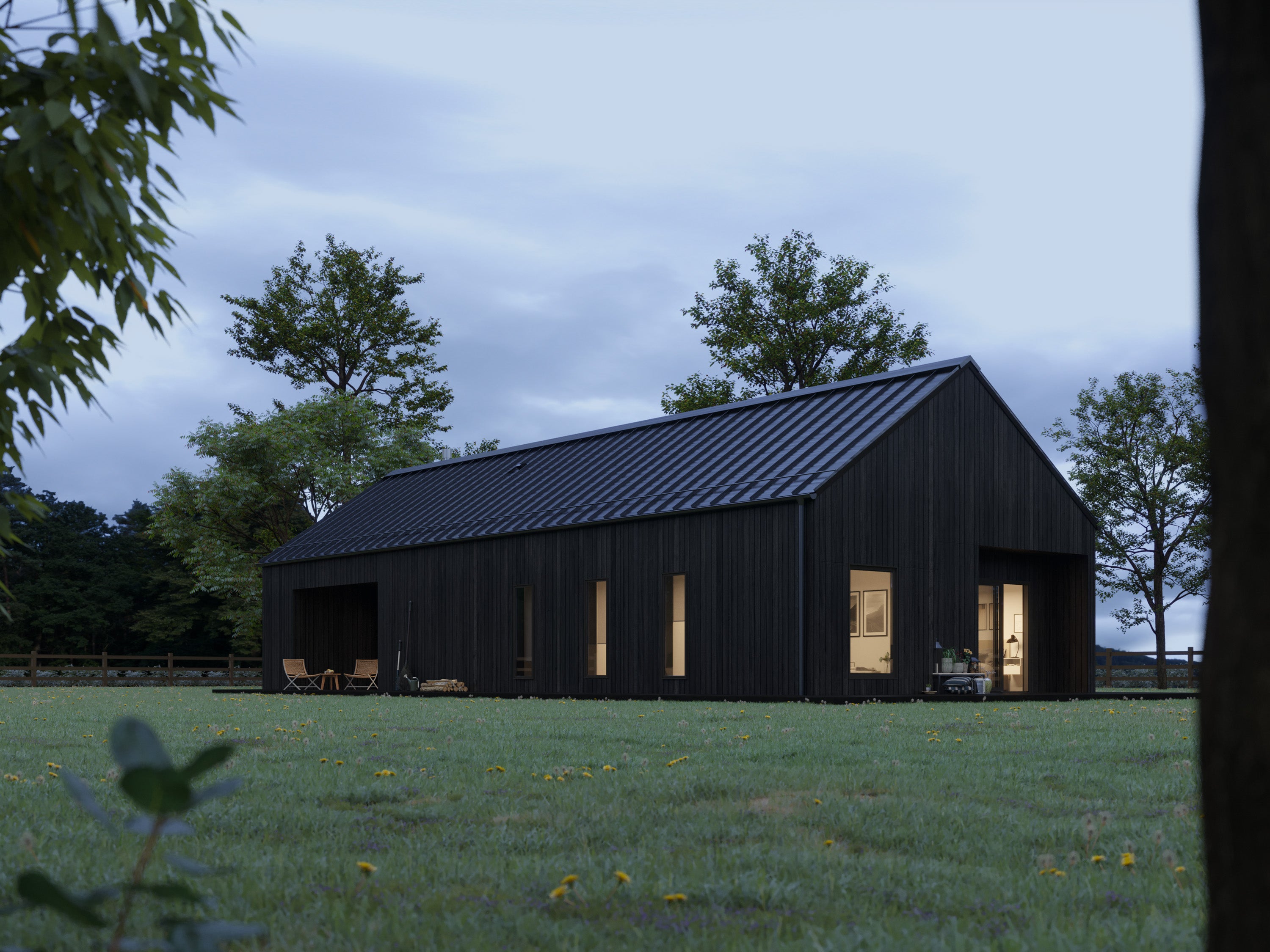 Black barn house with charred wood vertical cladding and pitched black metal roof at dusk, side elevation showing warm interior lighting through bedroom and living room windows against a moody twilight sky