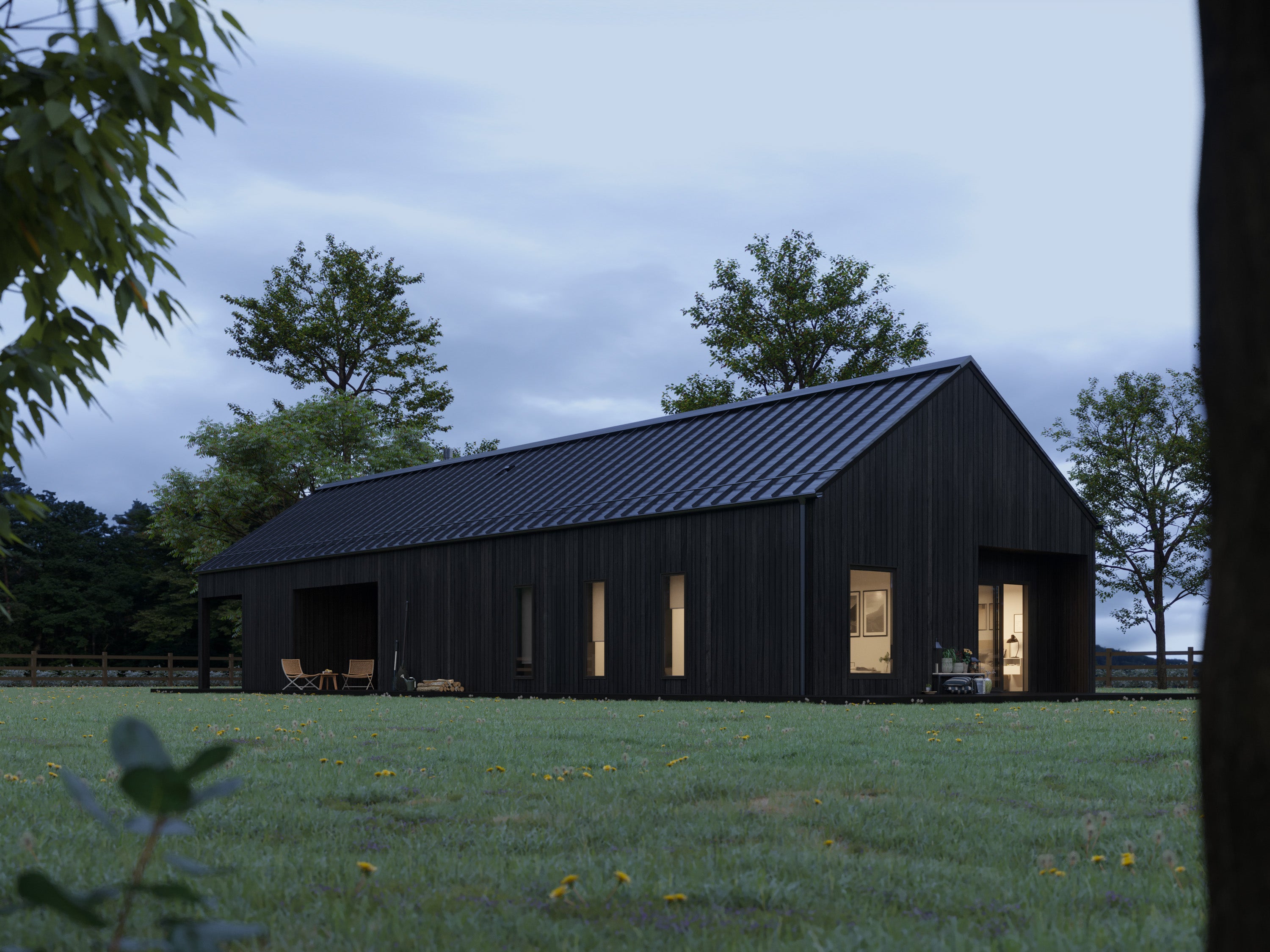 Black barn house with charred wood cladding and black standing seam metal roof at dusk, side elevation showing warm interior lighting through bedroom and living room windows