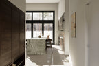 Modern home entry hallway looking into open kitchen with green marble island, floor-to-ceiling black-trim windows, and dark wood cabinetry – Design with Frank