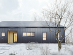 2-bedroom modern cabin house plan front elevation with wood entry accent, standing seam metal roof and siding, and warm interior lighting in winter