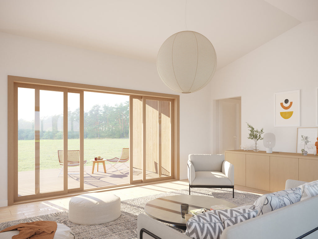Bright open-plan living room with vaulted white ceiling, large wood-framed sliding glass doors opening to a timber deck overlooking meadow, paper globe pendant light, and Scandinavian-style furniture