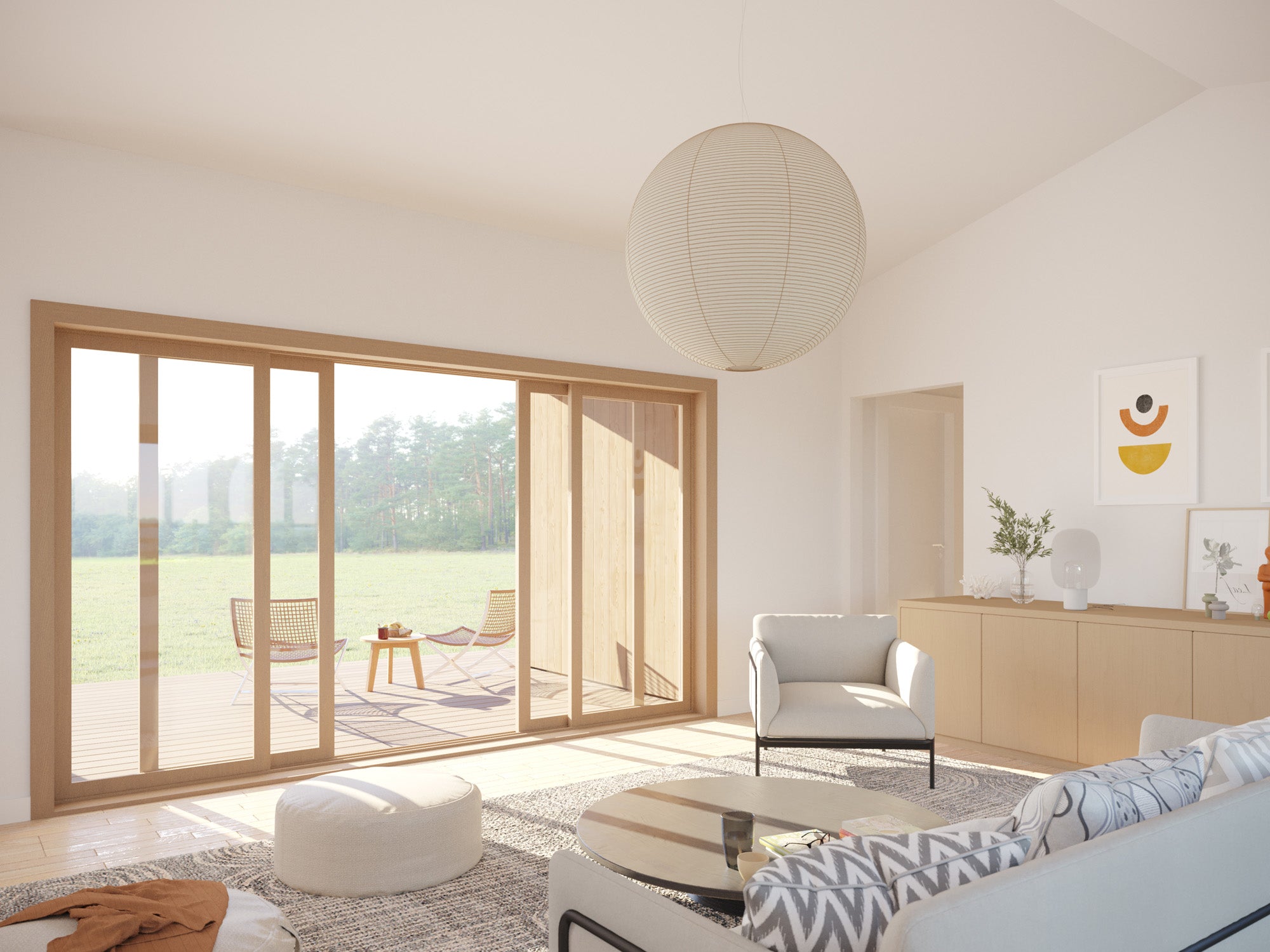 Bright open-plan living room with vaulted white ceiling, large wood-framed sliding glass doors opening to a timber deck overlooking meadow, paper globe pendant light, and Scandinavian-style furniture
