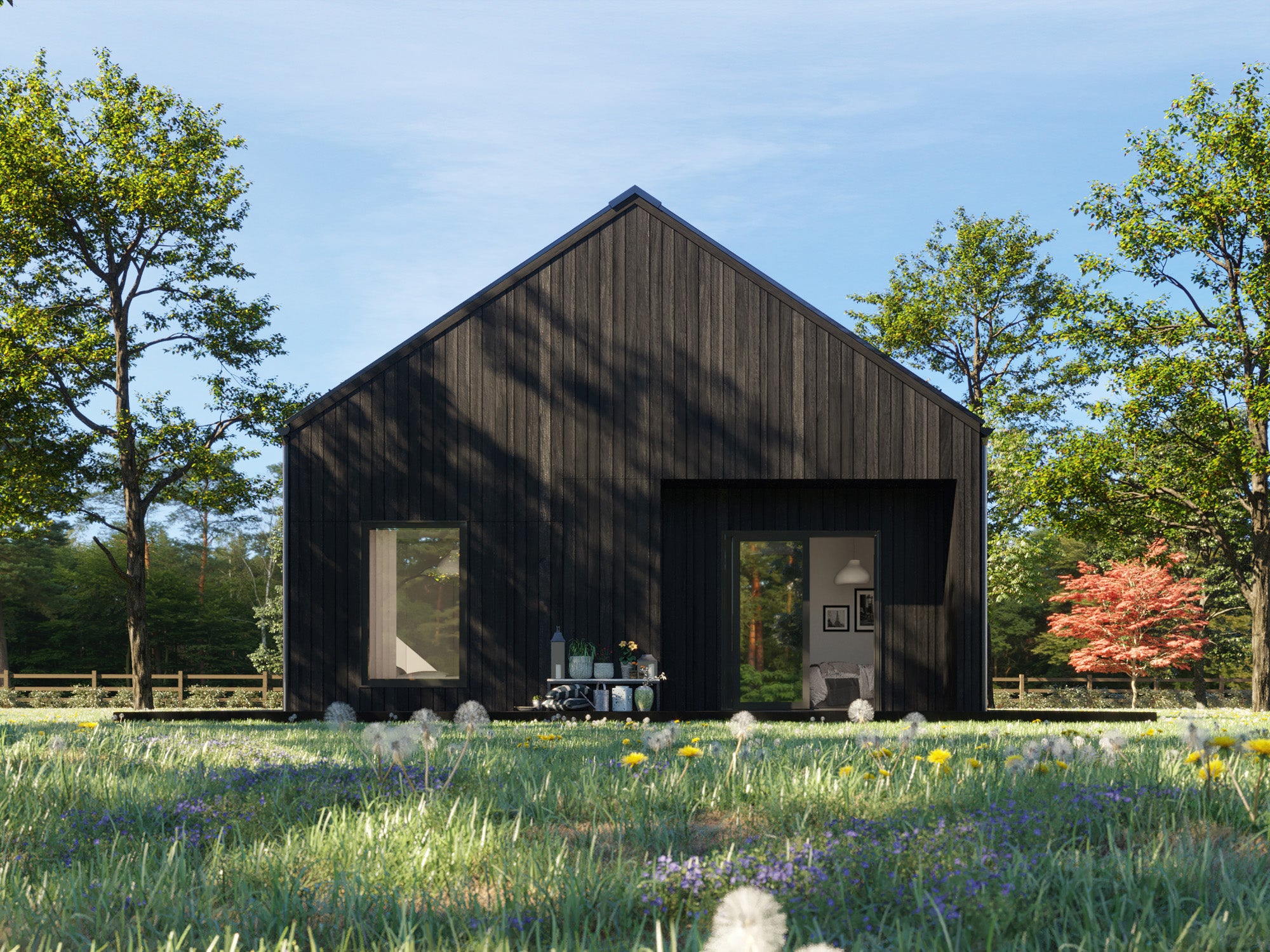  Small modern gable-end house with black charred wood vertical cladding, pitched roof, and recessed front entrance surrounded by wildflower meadow and mature trees